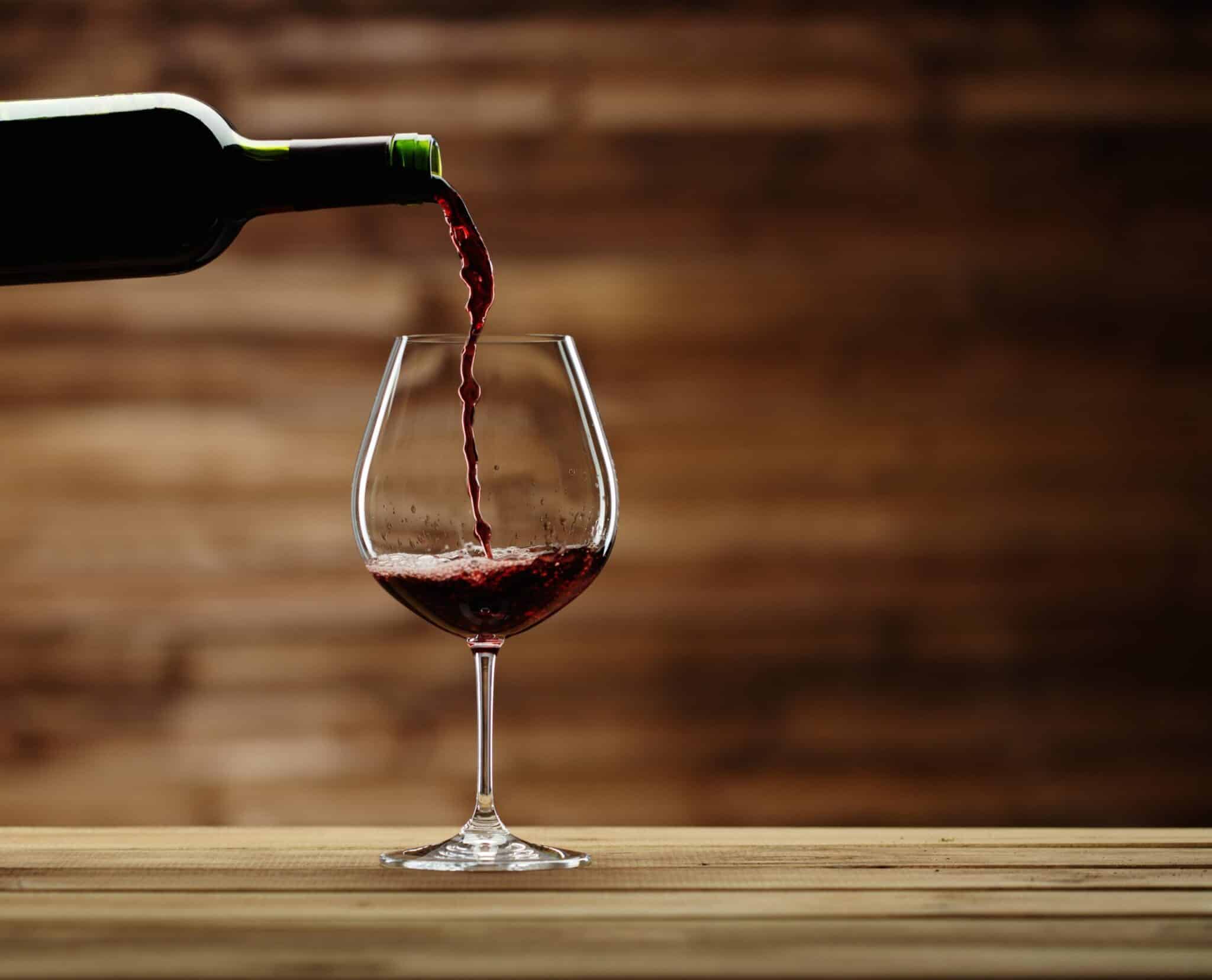 Pouring red wine into the glass against wooden background