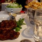 Steak frites on white plate and salad in white bowl with a white wine glass on white table cloth at Bistro Jeanty Restaurant in Yountvulle, CA, in the Napa Valley Wine Country; fine dining