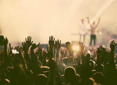 Large crowd of people raising their arms in the air at a concert with a band on the stage in the background in the Napa Valley Wine Country
