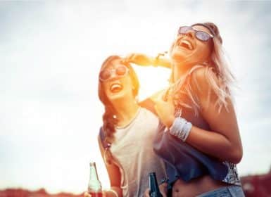 Two women laughing with beers in hand with sun shimmering behind them; Napa Valley, Wine Country