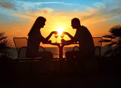 Couple outside on patio table and chair in front of ocean at sunset