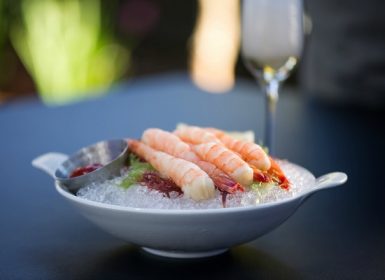 Shrimp over ice with ketchup condiment in white bowl on granite table outside with champagne in background; Napa Valley Wine Country