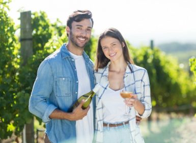 Couple embrace towards camera outside in front of vineyard holding rose wine glass and bottle in the Napa Valley Wine Country