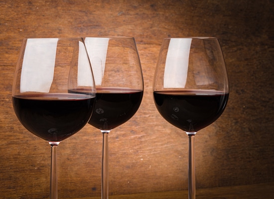 Three fine wine glasses half full with red wine over brown wooden background with spotlight effect; Wine Country, Napa Valley