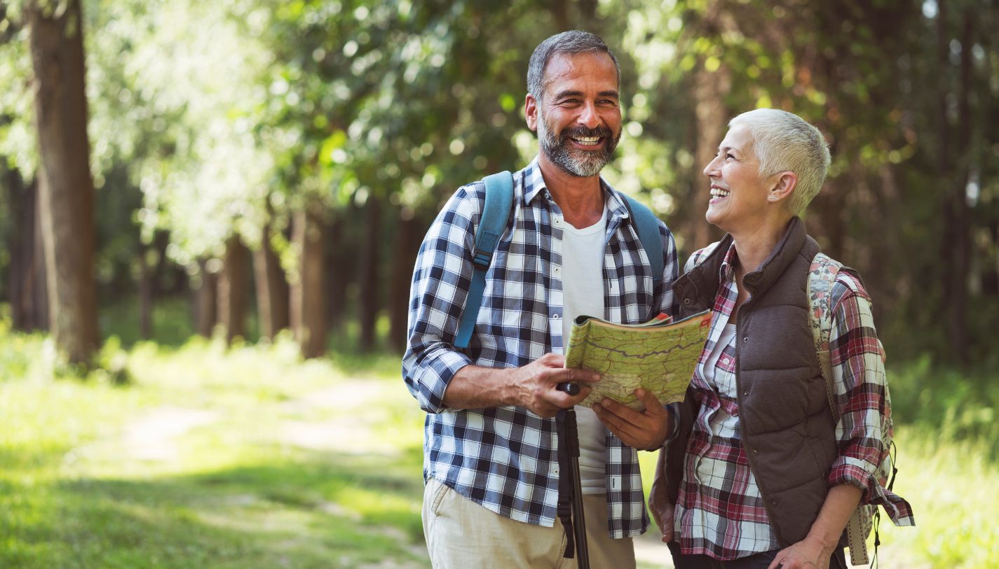 An older man and woman laughing as they hike in a forest
