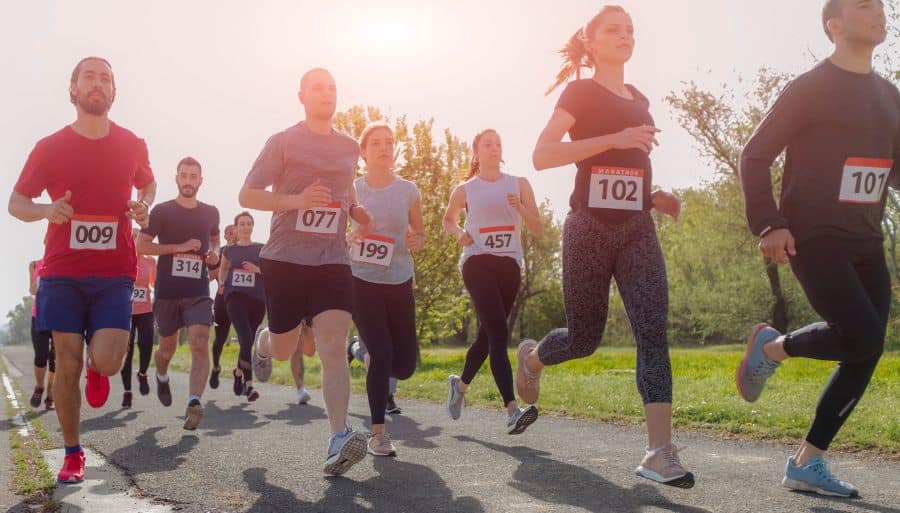a group of marathon runners running on a road with greenery in the background