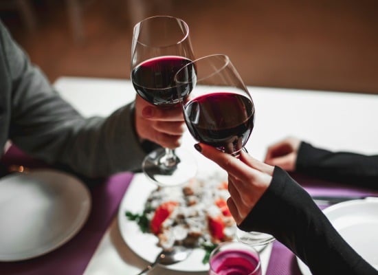 Two people clinking wine glasses while they share a meal.