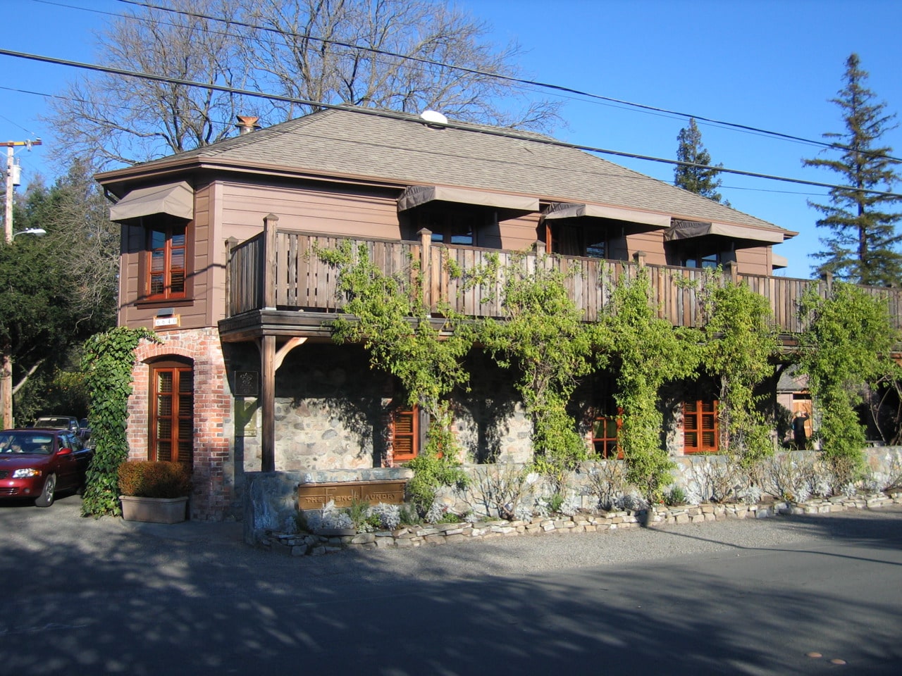 The outside view of the French Laundry, including stonework, siding, and a balcony with green vines growing along it.