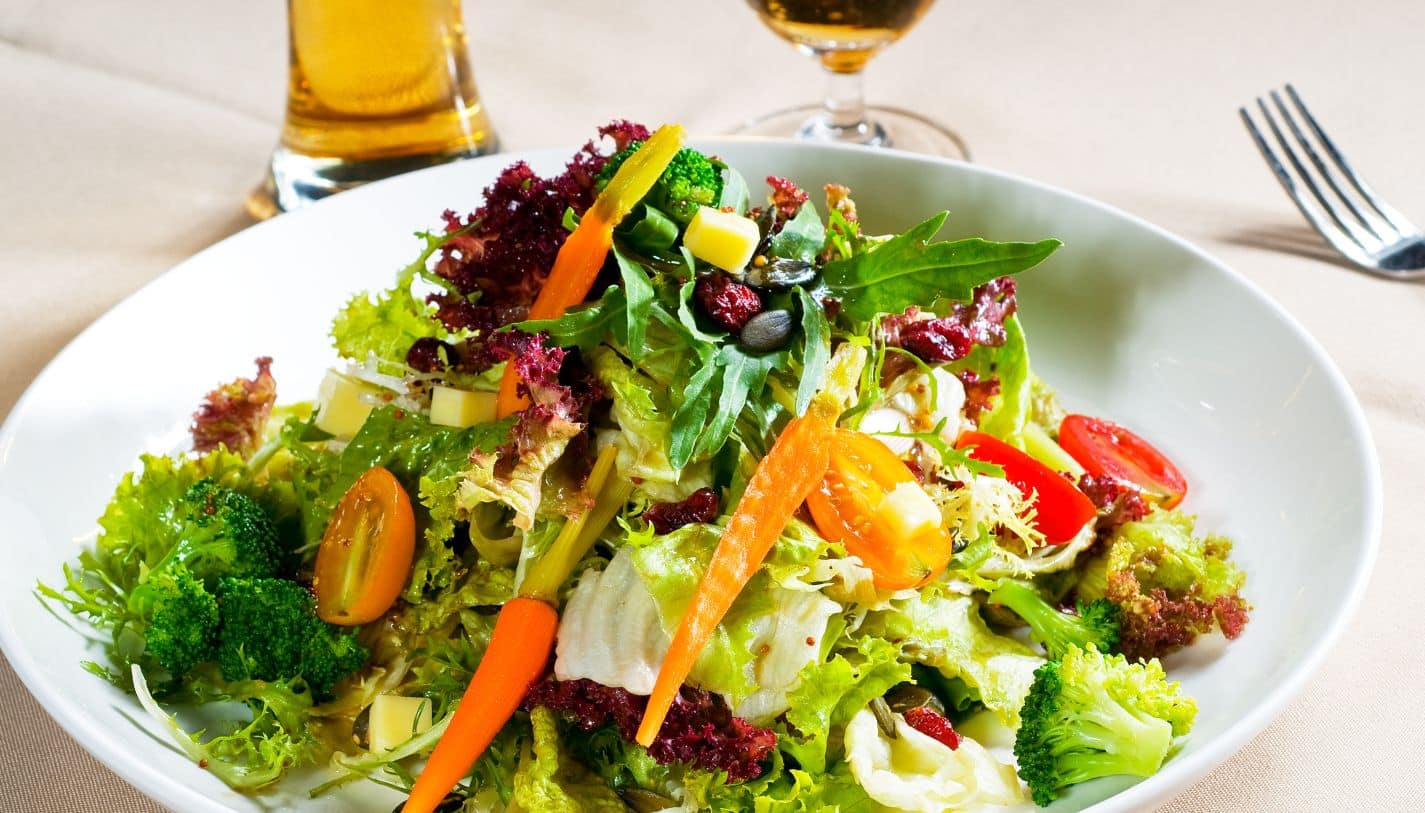 A fresh salad plated on a table with a fork and drink in the background