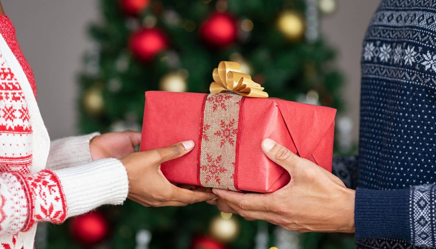 People exchanging gifts. A present with red wrapping paper and a gold bow between two people's hands.