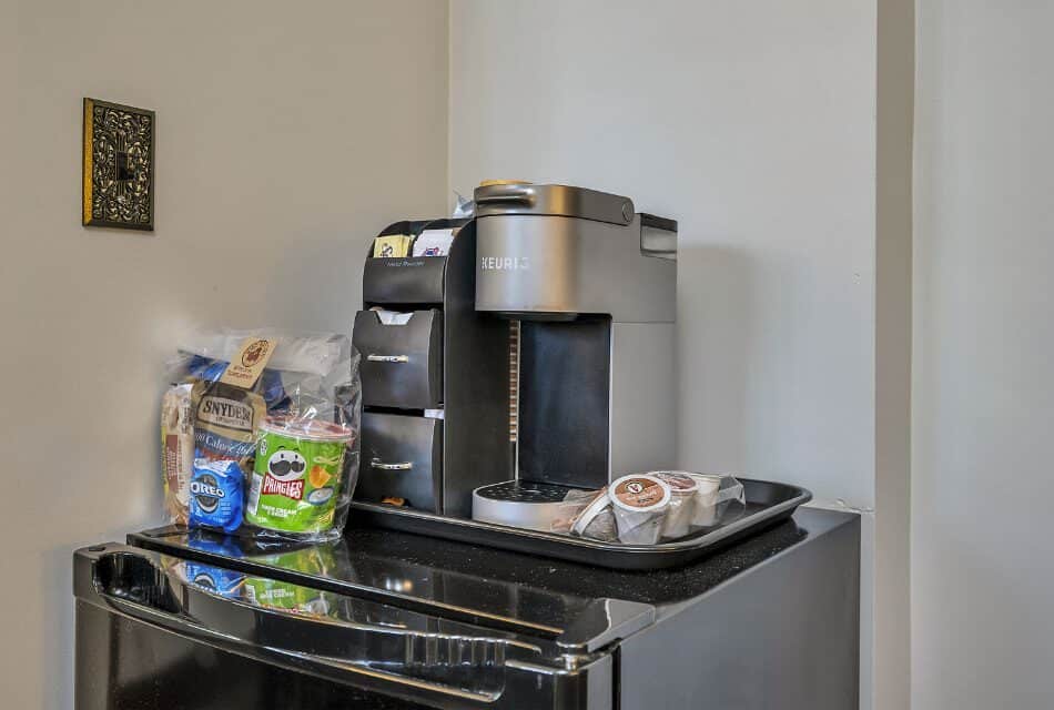 Keurig coffee maker and bag of snacks on top of black mini fridge