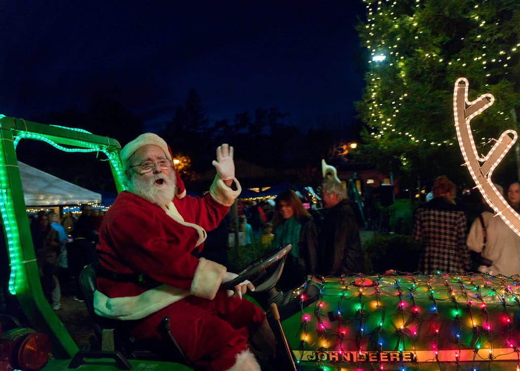 Santa Claus waves to crowds of people as he rides a decorated John Deere tractor through the Calistoga Lighted Christmas Parade.