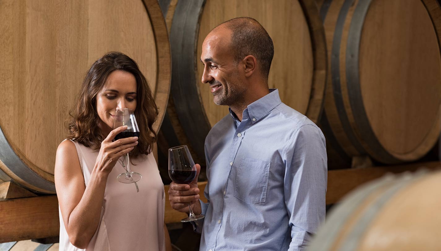 Romantic couple tasting a glass of red wine in a traditional cellar surrounded by wooden barrels.