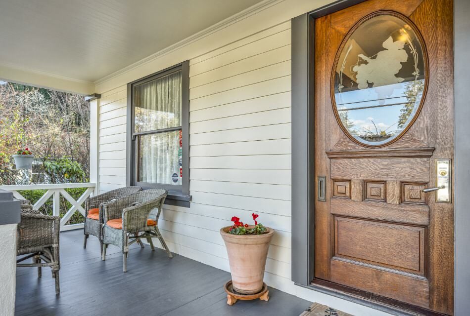 Exterior view of property's front porch painted white with gray trim, brown wood door, and gray wicker patio furniture