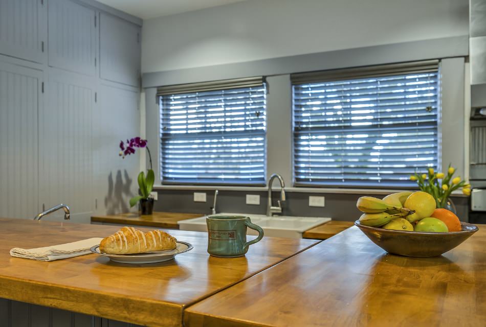Close up view of kitchen wooden counters with a pastry on a plate, stoneware mug, and bowl of fruit