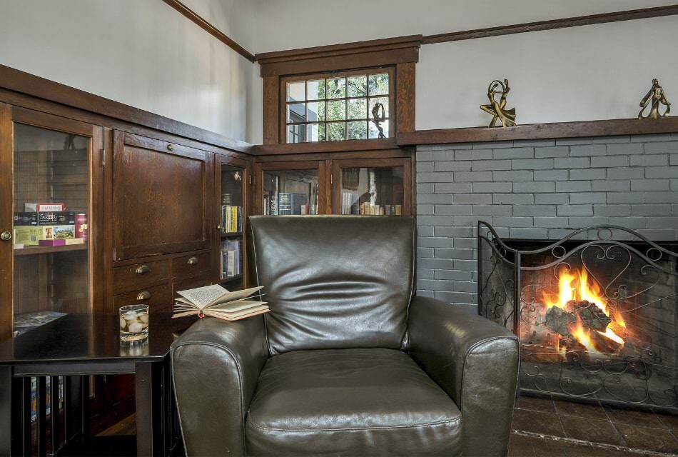 Close up view of dark brown leather armchair and wooden table next to a stone fireplace