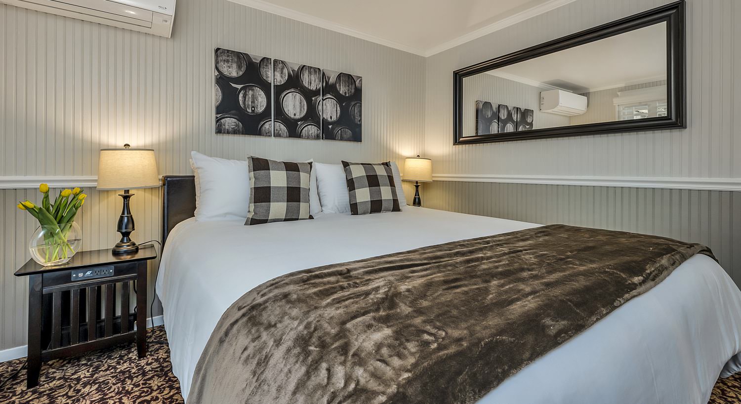 Bedroom with white walls, light gray wainscotting, floral carpeting, white bedding, and dark wooden nightstand