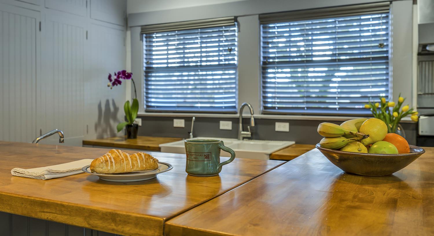 Close up view of kitchen wooden counters with a pastry on a plate, stoneware mug, and bowl of fruit