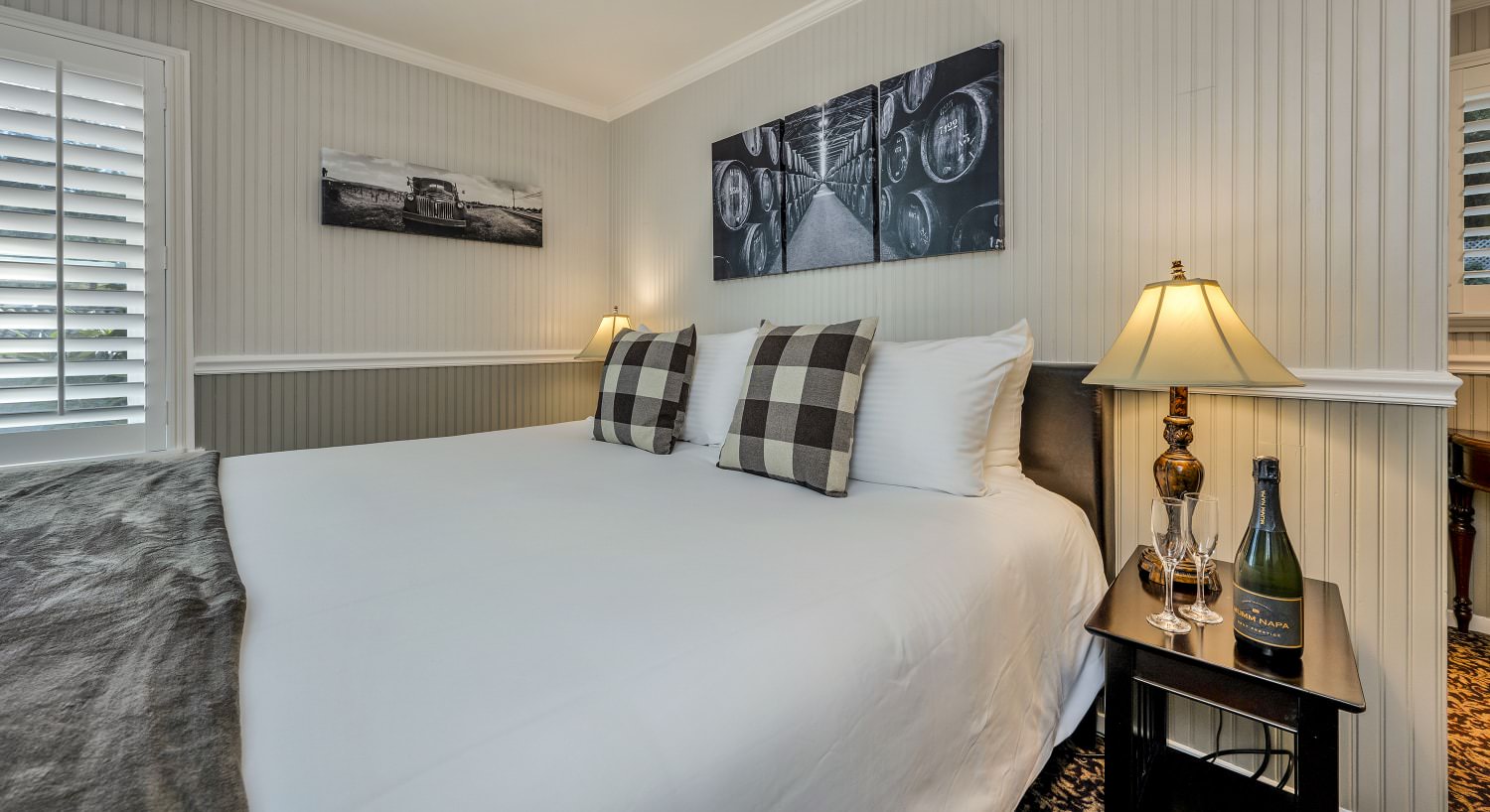 Bedroom with light white walls, light gray wainscotting, white bedding, and dark wooden nightstand