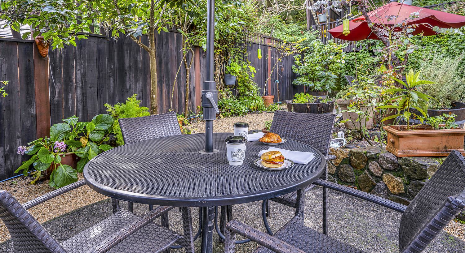 Metal patio table with one white plate with a breakfast bagel and another white plate with a chocolate filled croissant