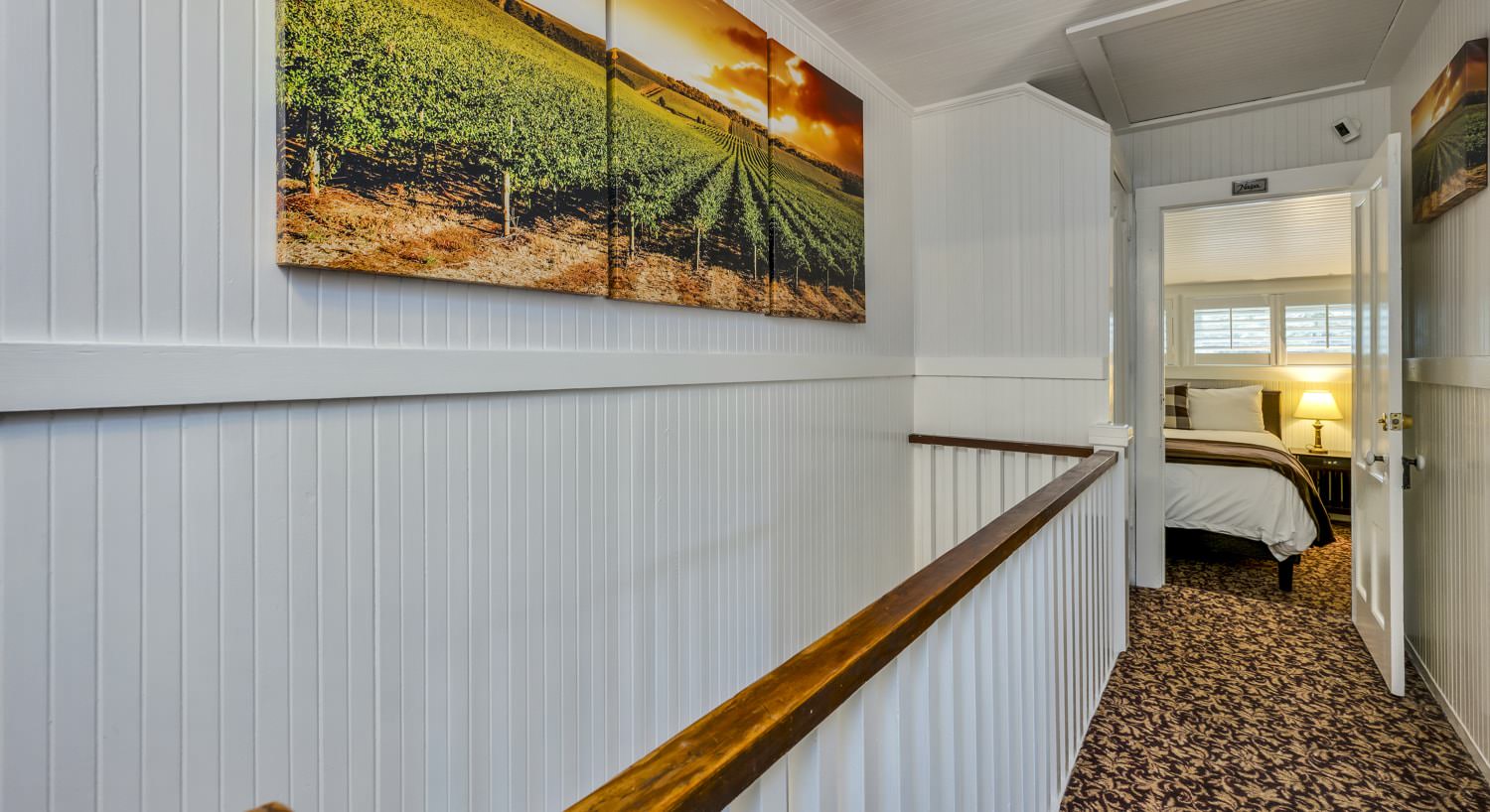 Hallway with white walls, floral carpeting, and open door to a bedroom