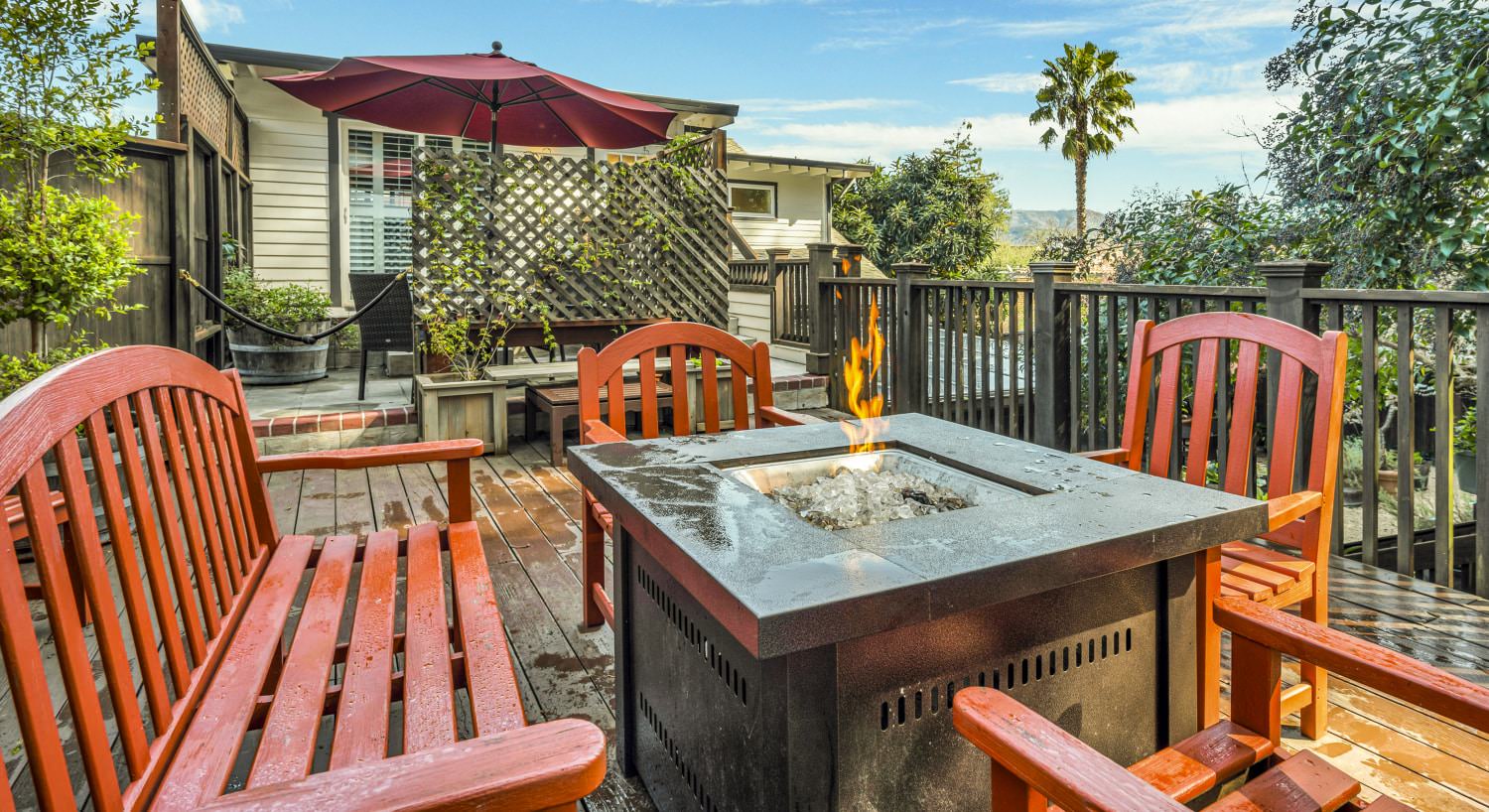 Orange wooden patio chairs and bench surrounding tabletop firepit on wooden deck