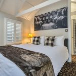 Bedroom with white walls, floral carpeting, white bedding, and view into closet with black mini fridge
