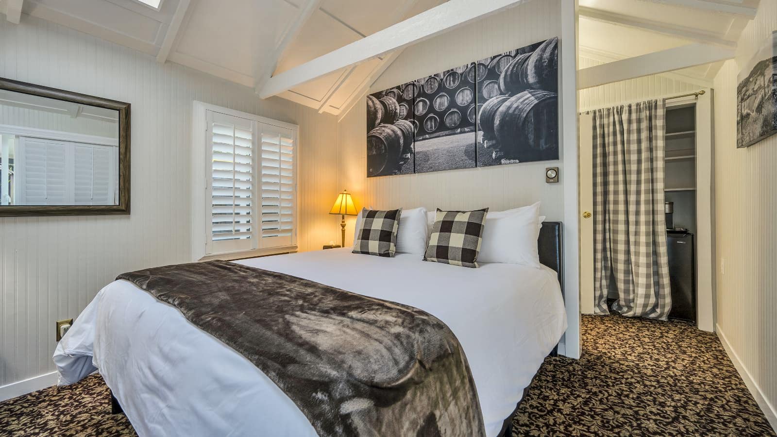 Bedroom with white walls, floral carpeting, white bedding, and view into closet with black mini fridge