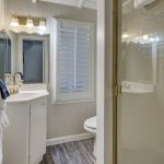 Bathroom with light gray walls, stand up shower, white toilet, and white vanity