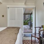 Bedroom with white walls, floral carpeting, white bedding, dark wooden table, and view out to back patio