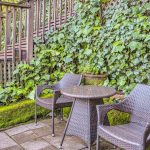 Stone patio with dark wicker chairs and table with lush green vegetation in the background