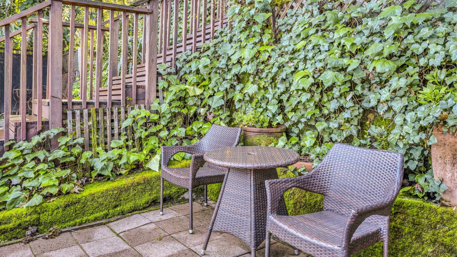 Stone patio with dark wicker chairs and table with lush green vegetation in the background
