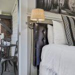 Close up view of leather upholstered headboard, white bedding, wall sconce, and view of metal patio table and chairs on balcony
