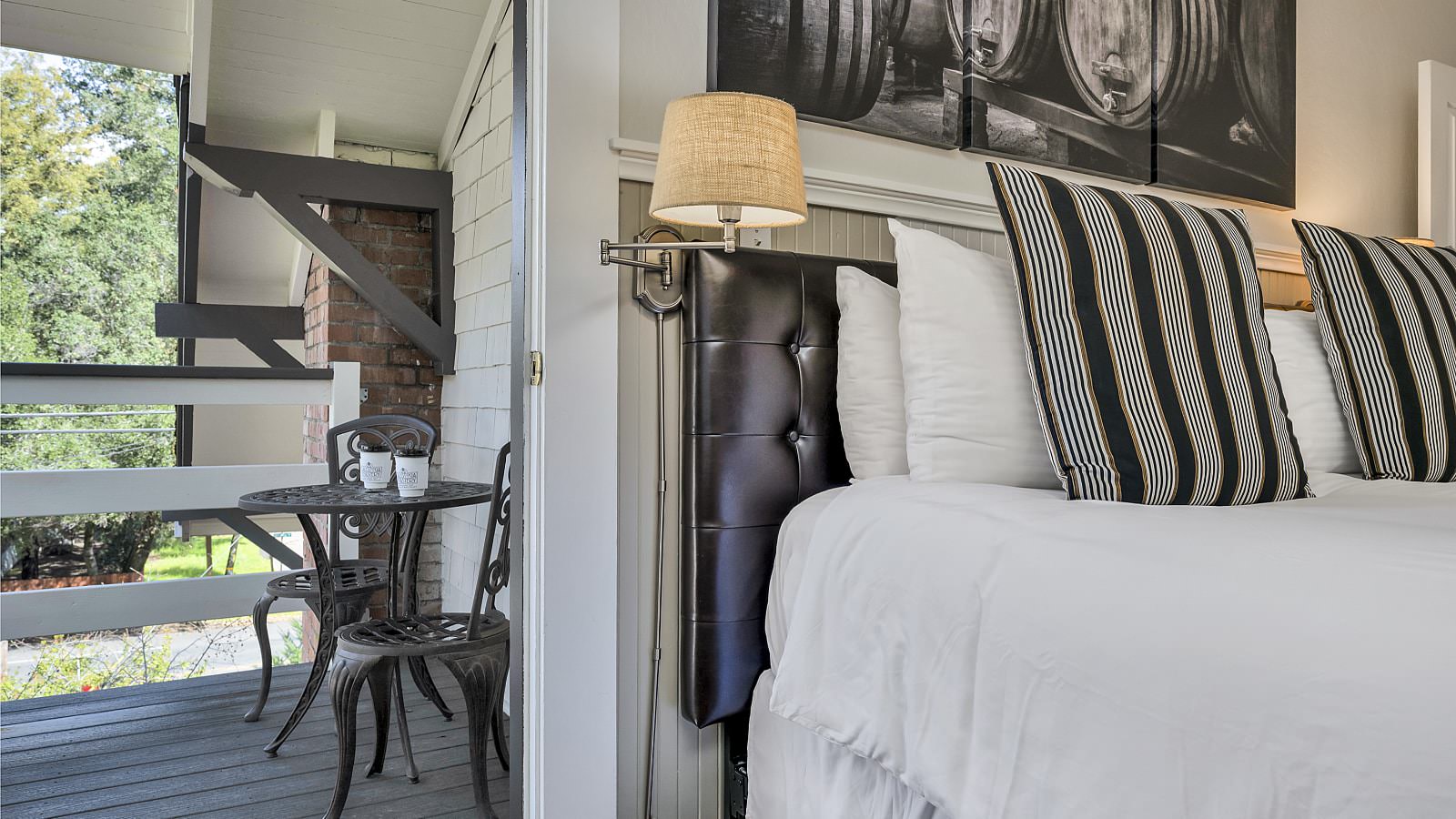 Close up view of leather upholstered headboard, white bedding, wall sconce, and view of metal patio table and chairs on balcony
