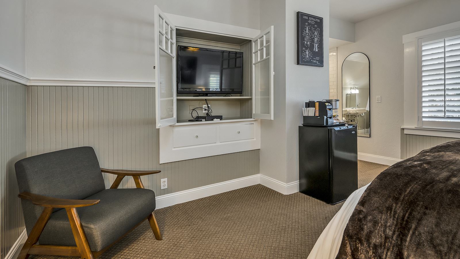 Bedroom with white walls, light gray wainscotting, light colored carpeting, white bedding, black mini fridge, and flatscreen TV