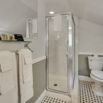 Bathroom with white walls, light gray wainscotting, black and white tiled floor, white toilet, white pedestal sink, and stand up shower