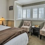 Bedroom with white walls, light gray wainscotting, light colored carpeting, white bedding, and sitting area