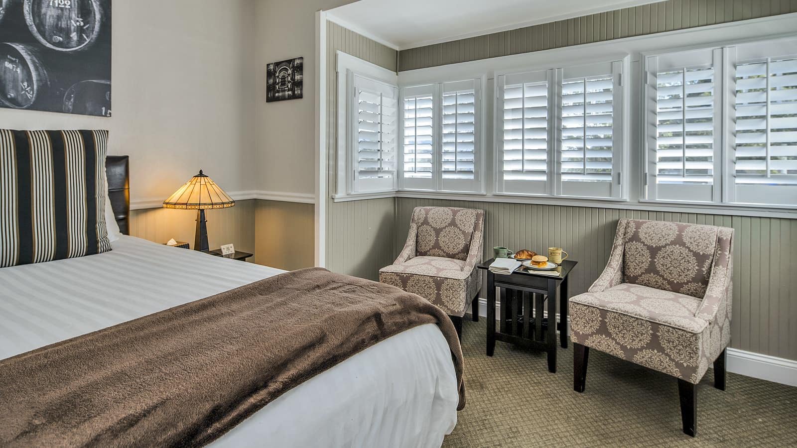 Bedroom with white walls, light gray wainscotting, light colored carpeting, white bedding, and sitting area