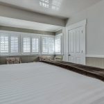Bedroom with white walls, light gray wainscotting, light colored carpeting, white bedding, and sitting area