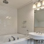 Bathroom with soaker tub surrounded by white tile and white pedestal sink