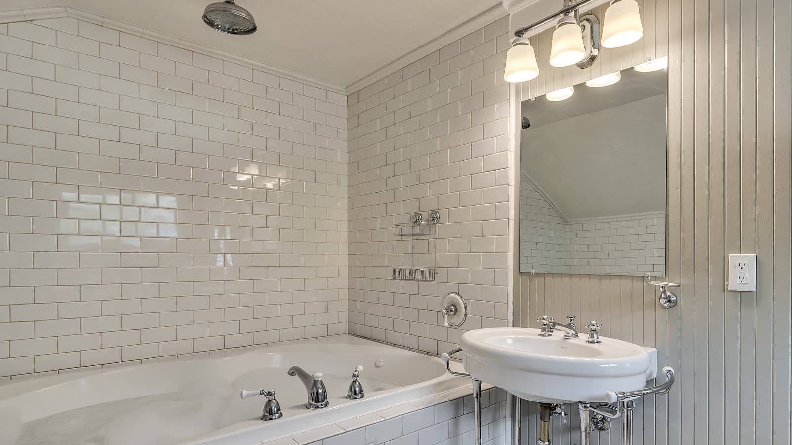 Bathroom with soaker tub surrounded by white tile and white pedestal sink
