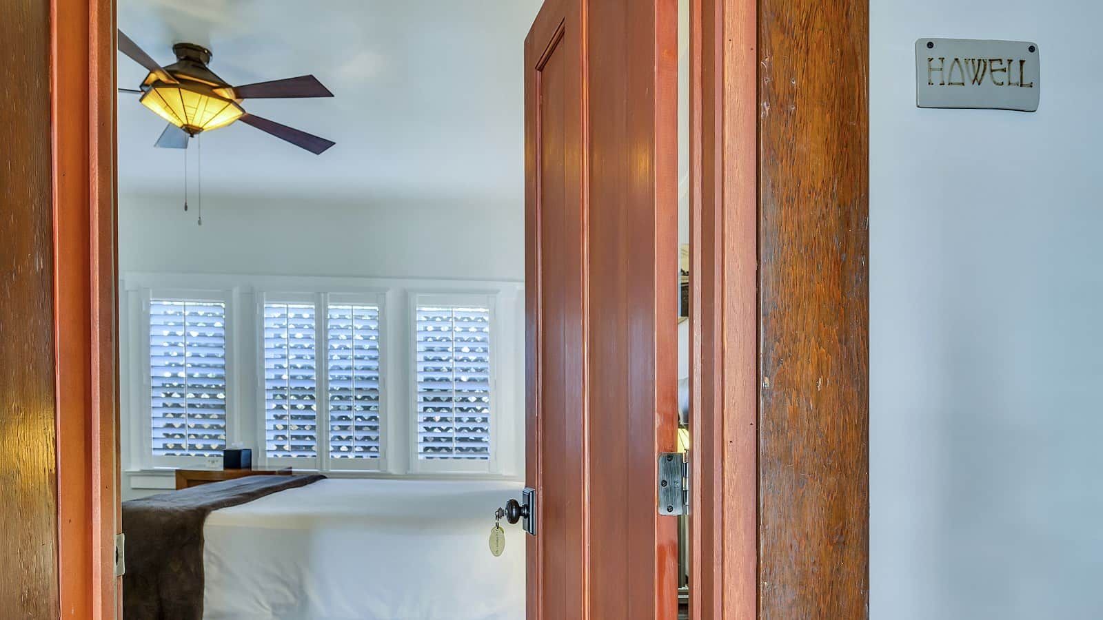 View into bedroom with white walls, white bedding, and dark wooden nightstand