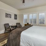 Bedroom with light gray and white walls, hardwood flooring, white bedding, and sitting area