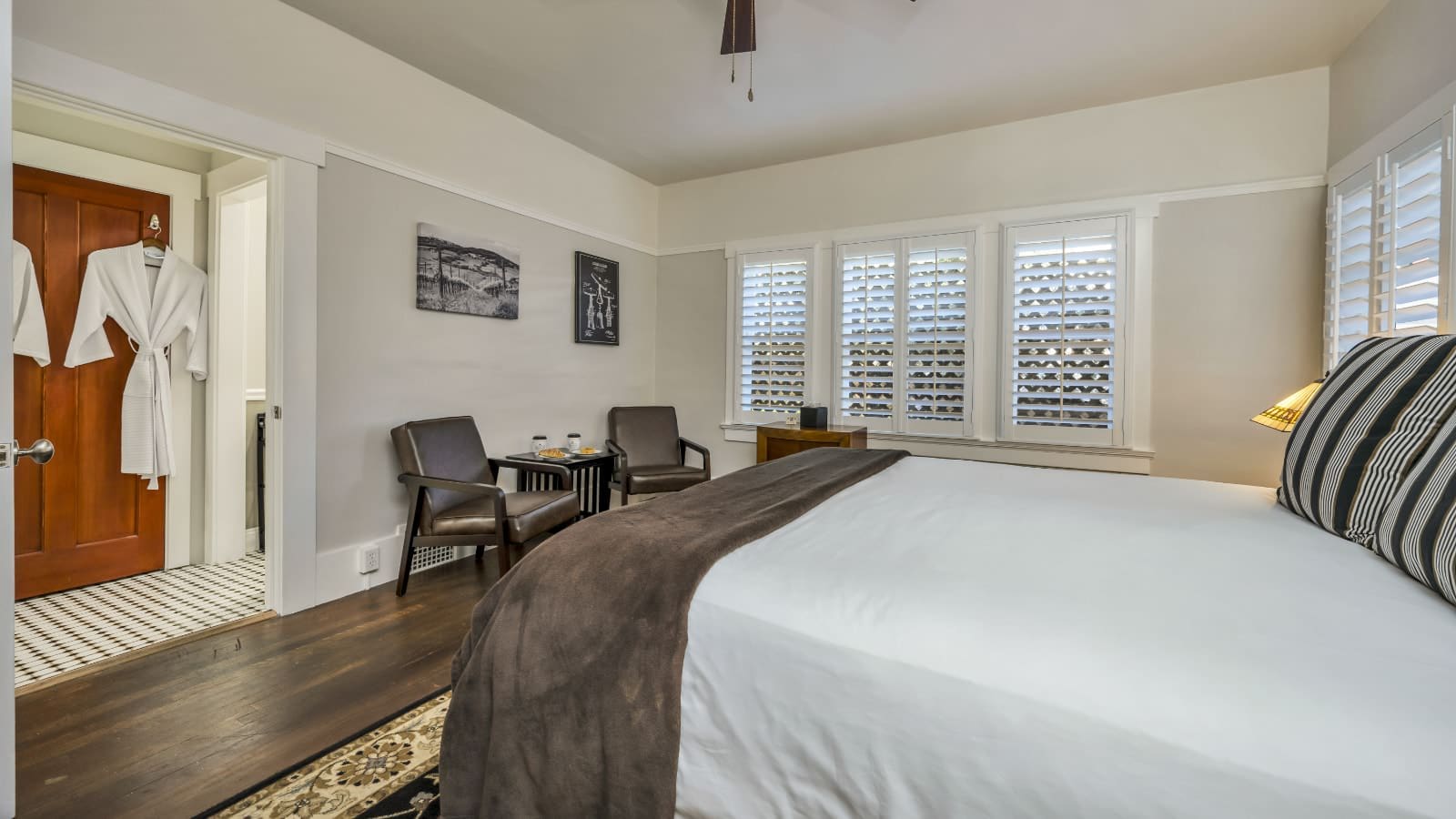 Bedroom with light gray and white walls, hardwood flooring, white bedding, and sitting area