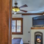 View into bedroom with white walls, light colored carpeting, white bedding, leather bed bench, and electric fireplace