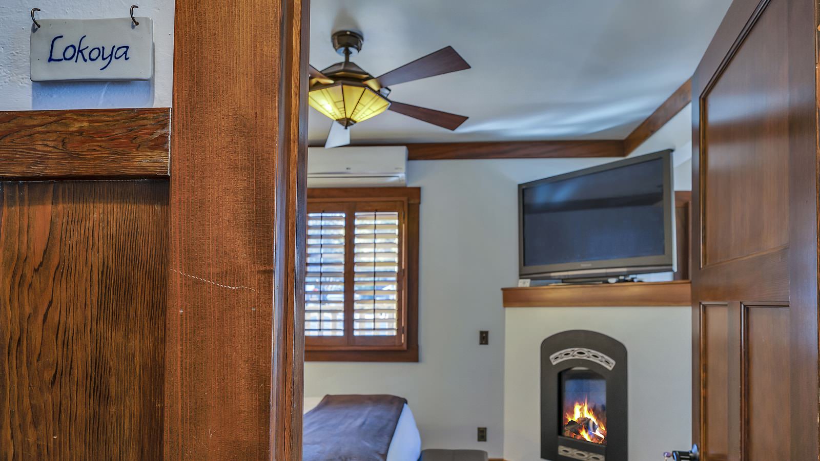 View into bedroom with white walls, light colored carpeting, white bedding, leather bed bench, and electric fireplace
