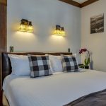 Bedroom with white walls, light colored carpeting, white bedding, and view into bathroom