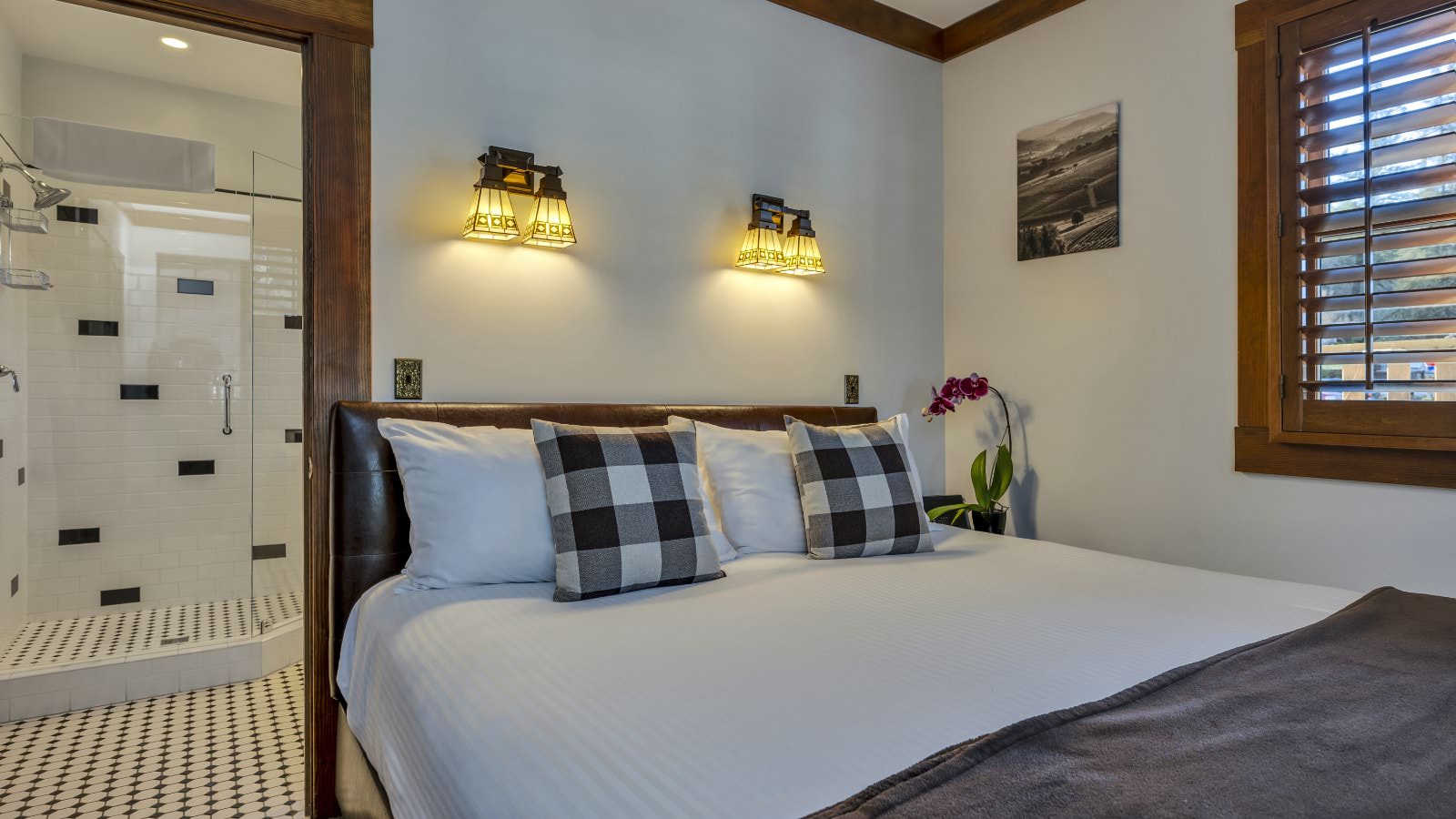 Bedroom with white walls, light colored carpeting, white bedding, and view into bathroom