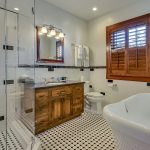 Bathroom with white walls, black and white tiled floor, dark wooden vanity, black and white tiled shower, and white clawfoot tub