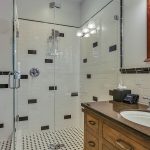 Bathroom with white walls, black and white tiled floor, dark wooden vanity, and black and white tiled shower